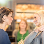 A middle-aged woman wearing a SONNET 2 audio processor for her cochlear implant has a conversation with a friend in a grocery store--benefiting from binaural hearing.