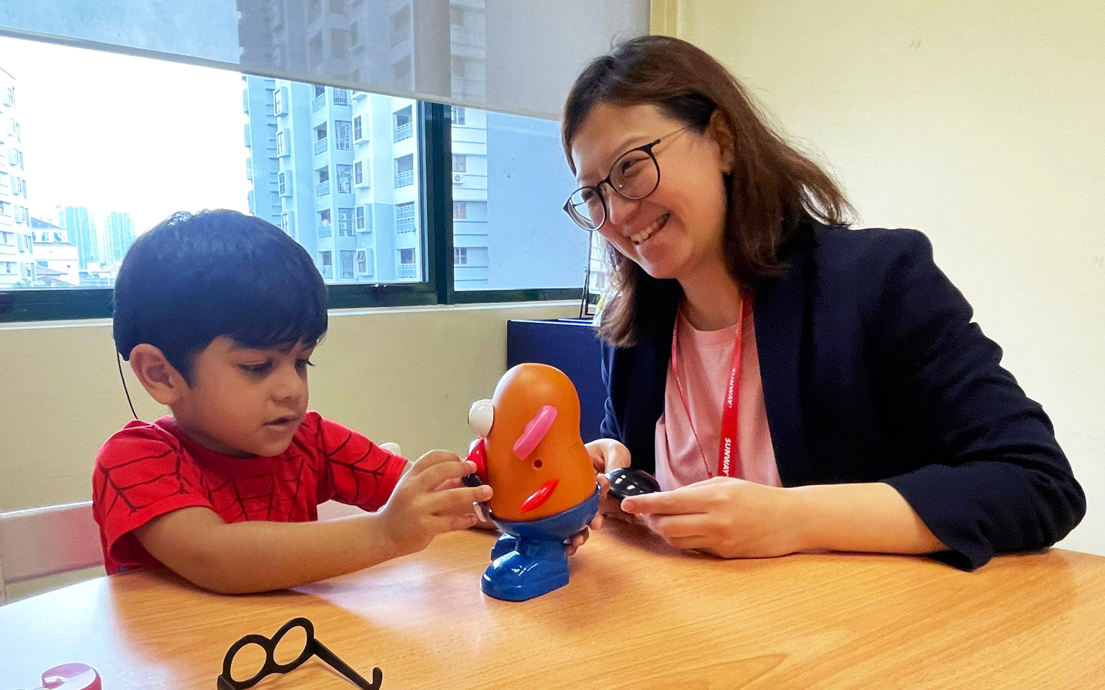 A three-year-old boy named Jaiden plays as his speech-language therapist smiles.