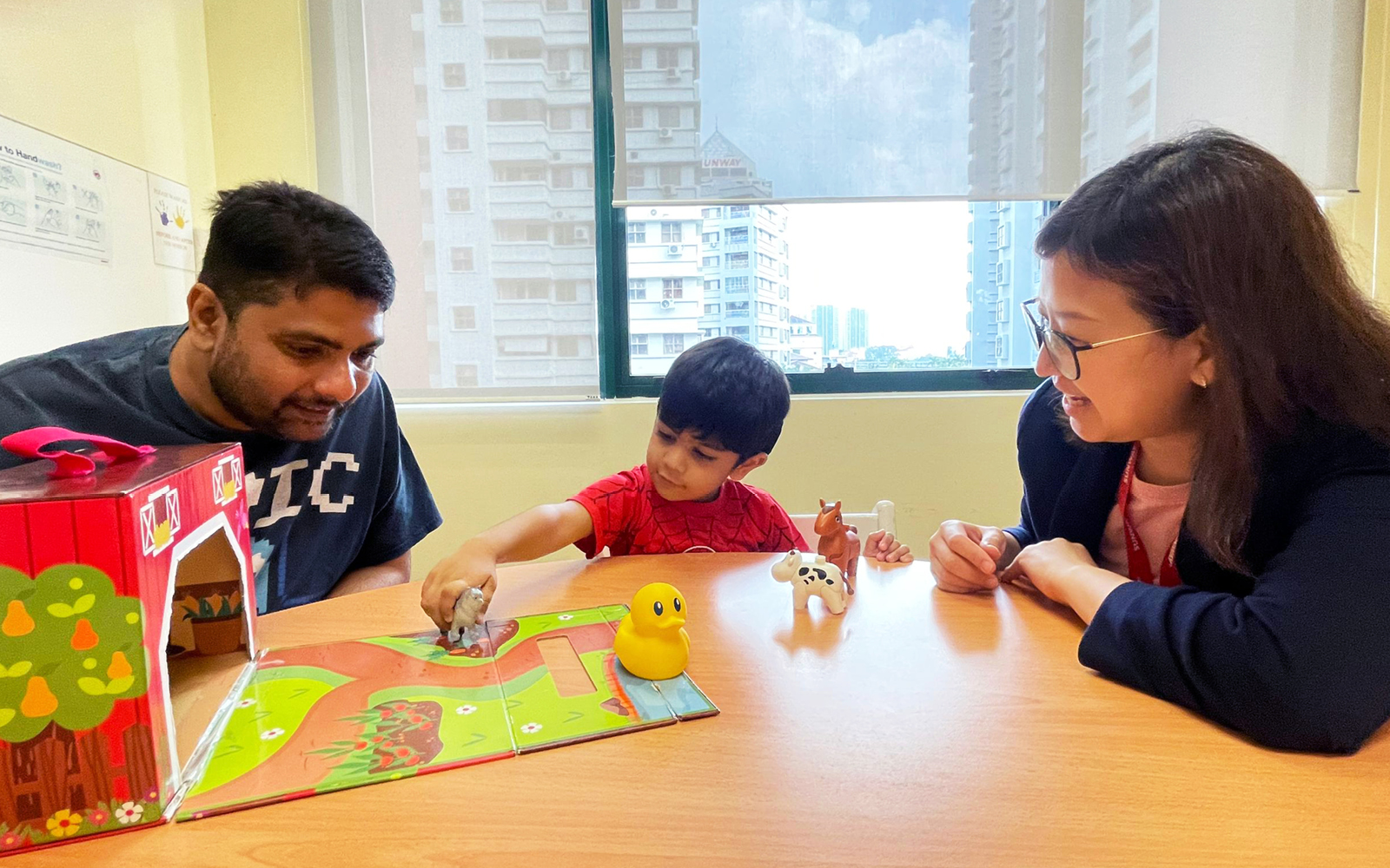 A young boy plays with barnyard figures as his father and speech-language therapist work with him to overcome inconsistent auditory skills.