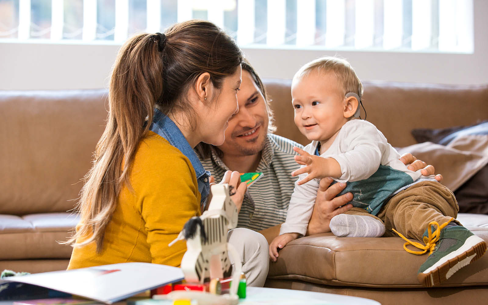 A woman and man speak and play with a very young child. It is important to continue working between therapy sessions with these Strategies to Develop Listening Skills & Speech.