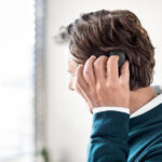 A man places the RONDO 3 audio processor on the side of his head under his hair as his audiologist explains how it works to him.