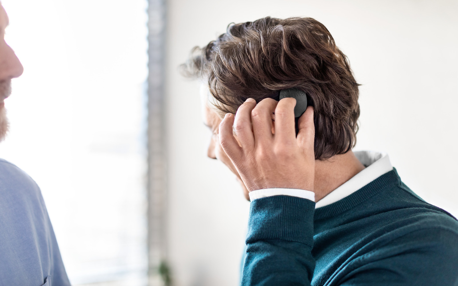 A man places the RONDO 3 audio processor on the side of his head under his hair as his audiologist explains how it works to him.