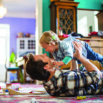 Man holding a child with a woman in the back.