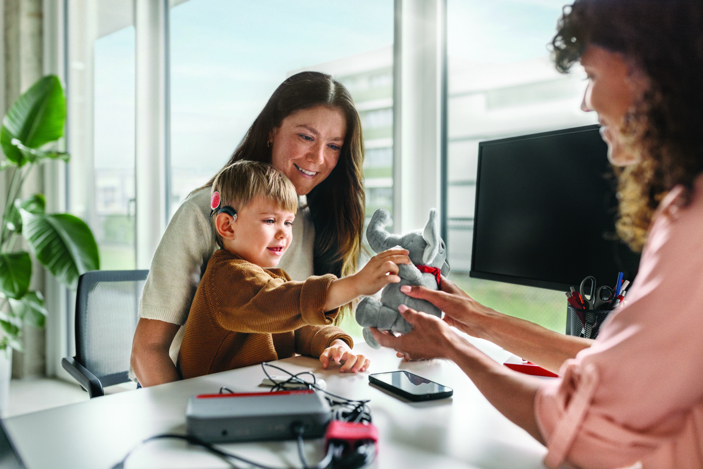 Woman holding child with a stuffed animal and another woman.
