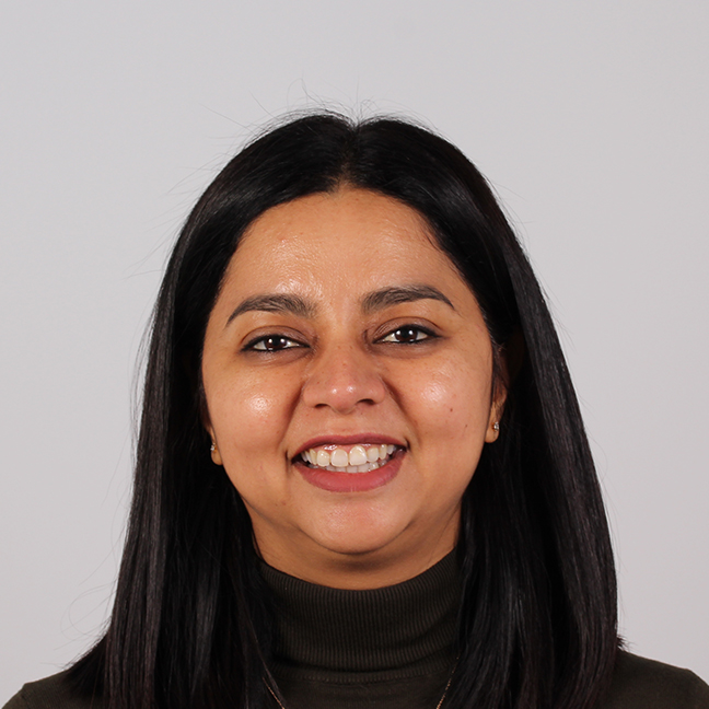 A woman with straight, shoulder‑length dark hair is shown against a plain light background, wearing a dark turtleneck top and a small earring.