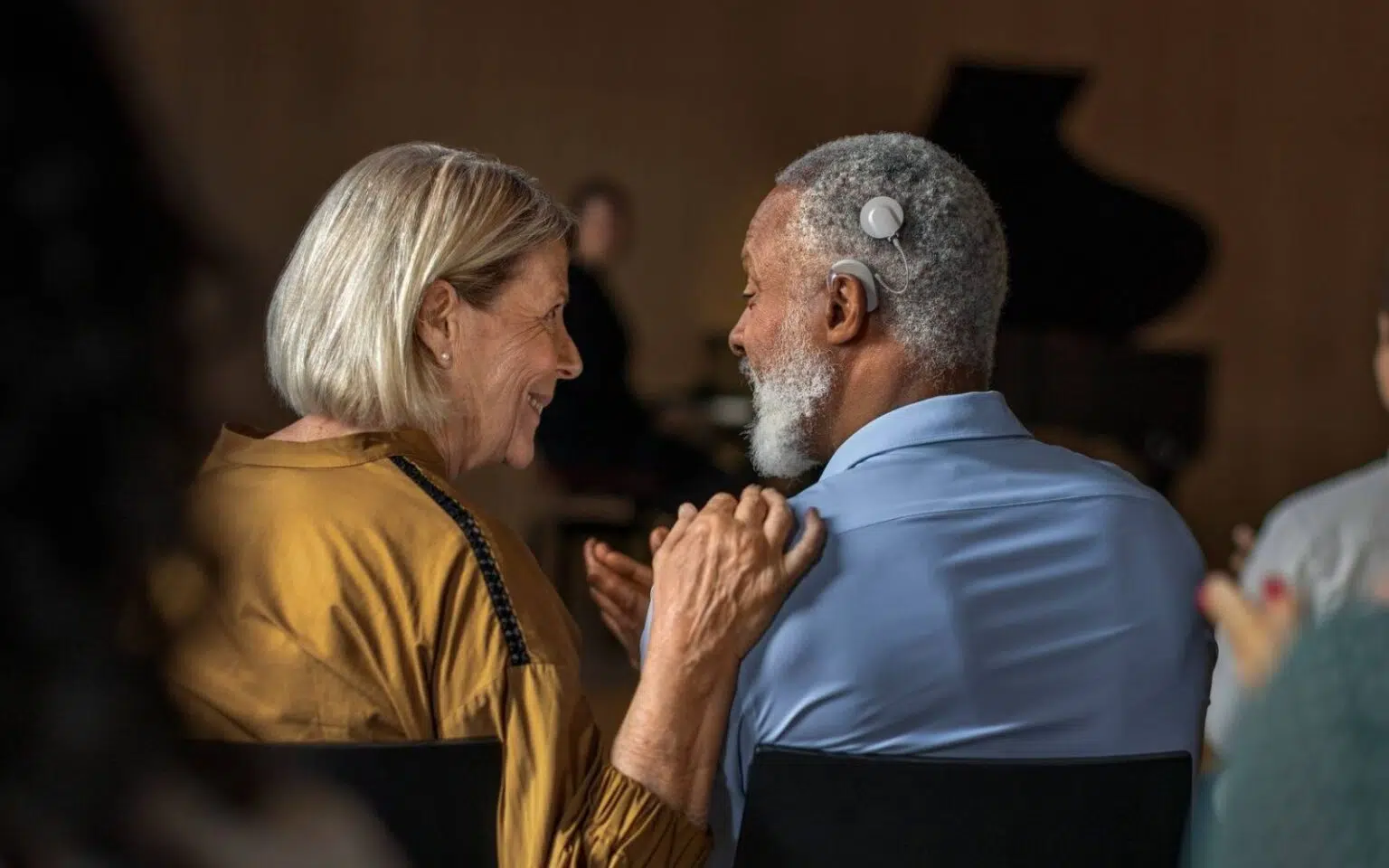 A woman on the left places her hand on the shoulder of the man on the right who has a cochlear implant